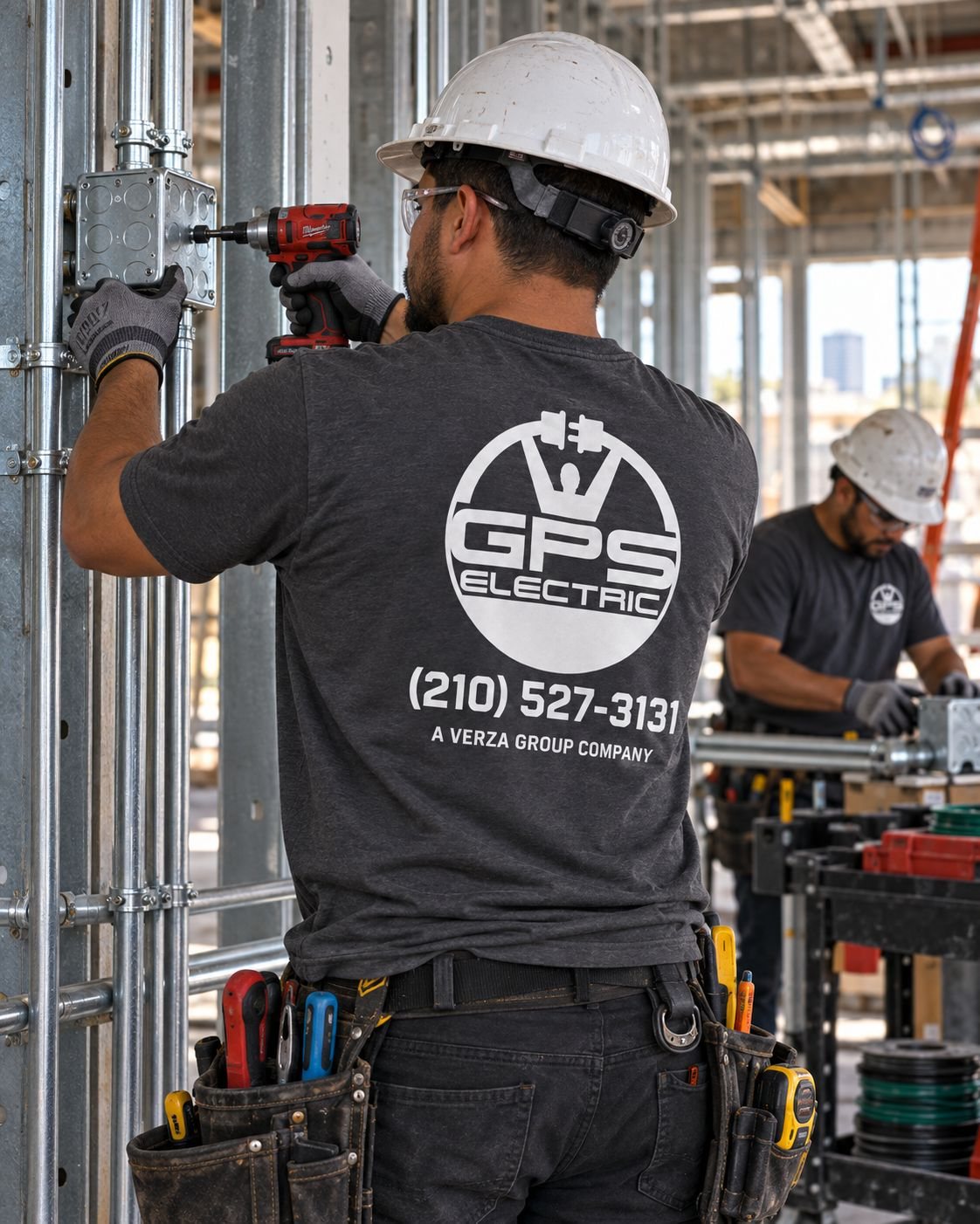 GPS Electric electrician fastening a junction box to steel conduit on a commercial job site, GPS Electric logo and phone number printed on his shirt